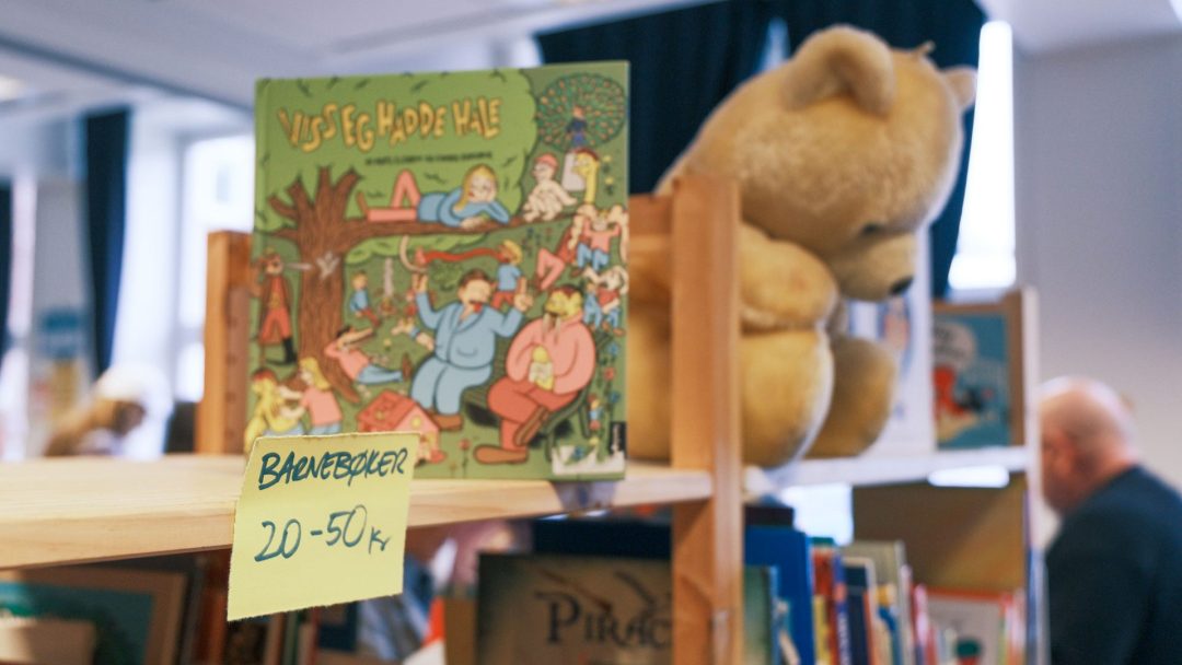 Barnebok utstilt i en hylle med bamse og prislapp på Barnebøker 20-50kr på loppemarked