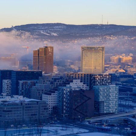 Luftfoto av et storbyer bybilde med moderne bygninger, en fjern tåkete horisont og et snødekt område i forgrunnen, som gjenspeiler gjennomtenkt planlegging innenfor klimabudsjettet.