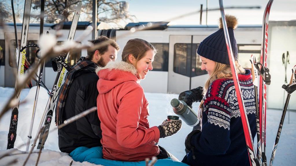 tre unge voksne med ski drikker kaffe fra termos på en t-banestasjon. Foto: Ruter, Birdy, Birgitte Heneide