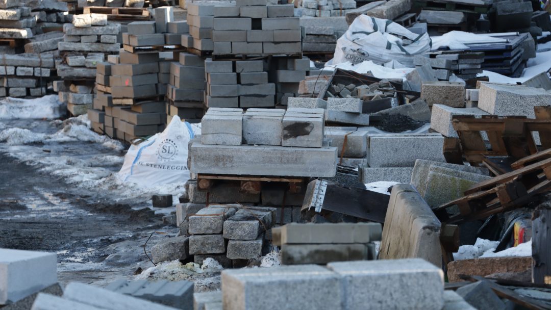 Stabler av stein og Stein betongblokker i forskjellige størrelser, noen pakket inn i plast, er pent arrangert i et utendørs lagringsområde.