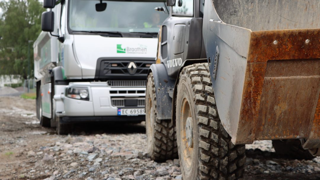 En Byene dumper og en hvit lastebil dominerer den steinete byggeplassen, imponerende sett fra lav vinkel.